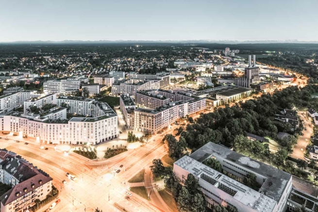 Drohnenfotografie einer Kreuzung, Wohnanlage und Alpenpanorama in der Abenddämmerung
