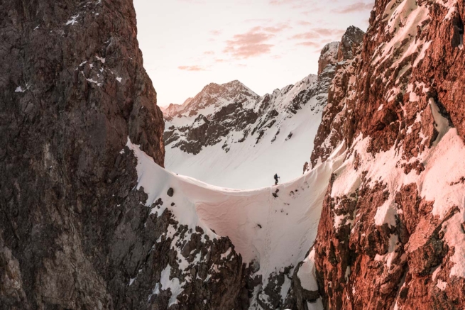 Skitourengeher bei Sonnenaufgang in einem Sattel, zwischen Felsen