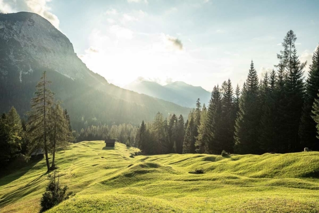 Sonnenuntergang über einer Bergwiese und Almhütten zwischen Wald und Felswänden bei Ehrwald, Tirol.