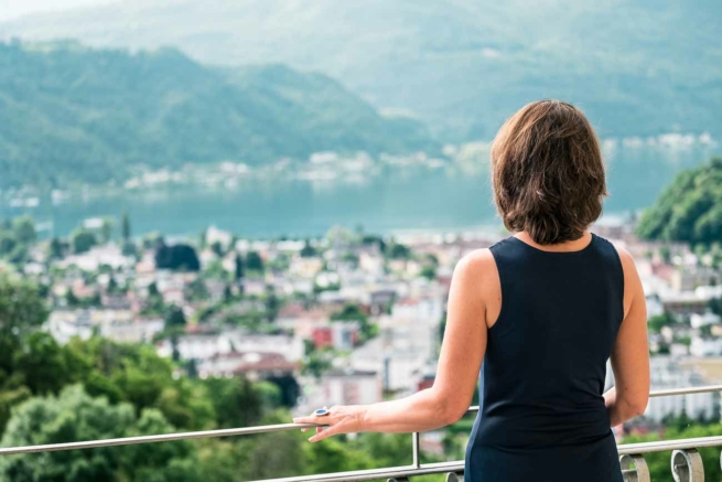 Eine Frau blickt vom Balkon ihres Hotelzimmers über den Luganer See.