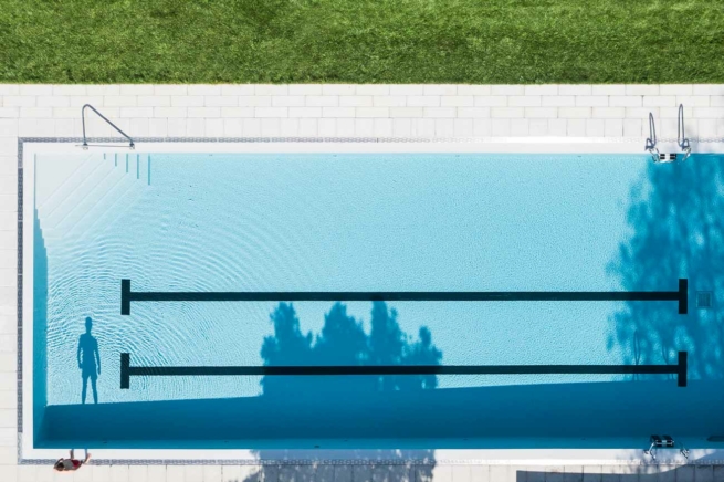 Ein Mann wirft einen langen Schatten in der Morgensonne in den Pool des Hotels.